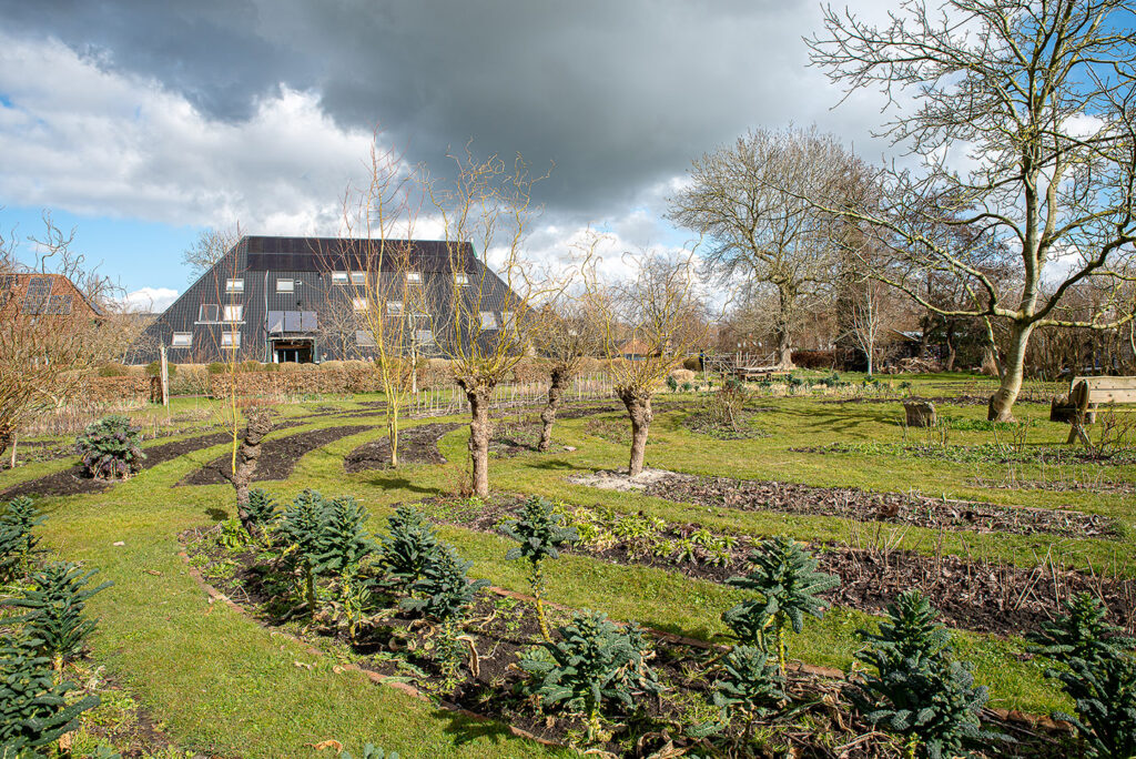 Op de voorgrond een grote tuin met bomen. Op de achtergrond is stadsboerderij De Wiershoeck te zien.